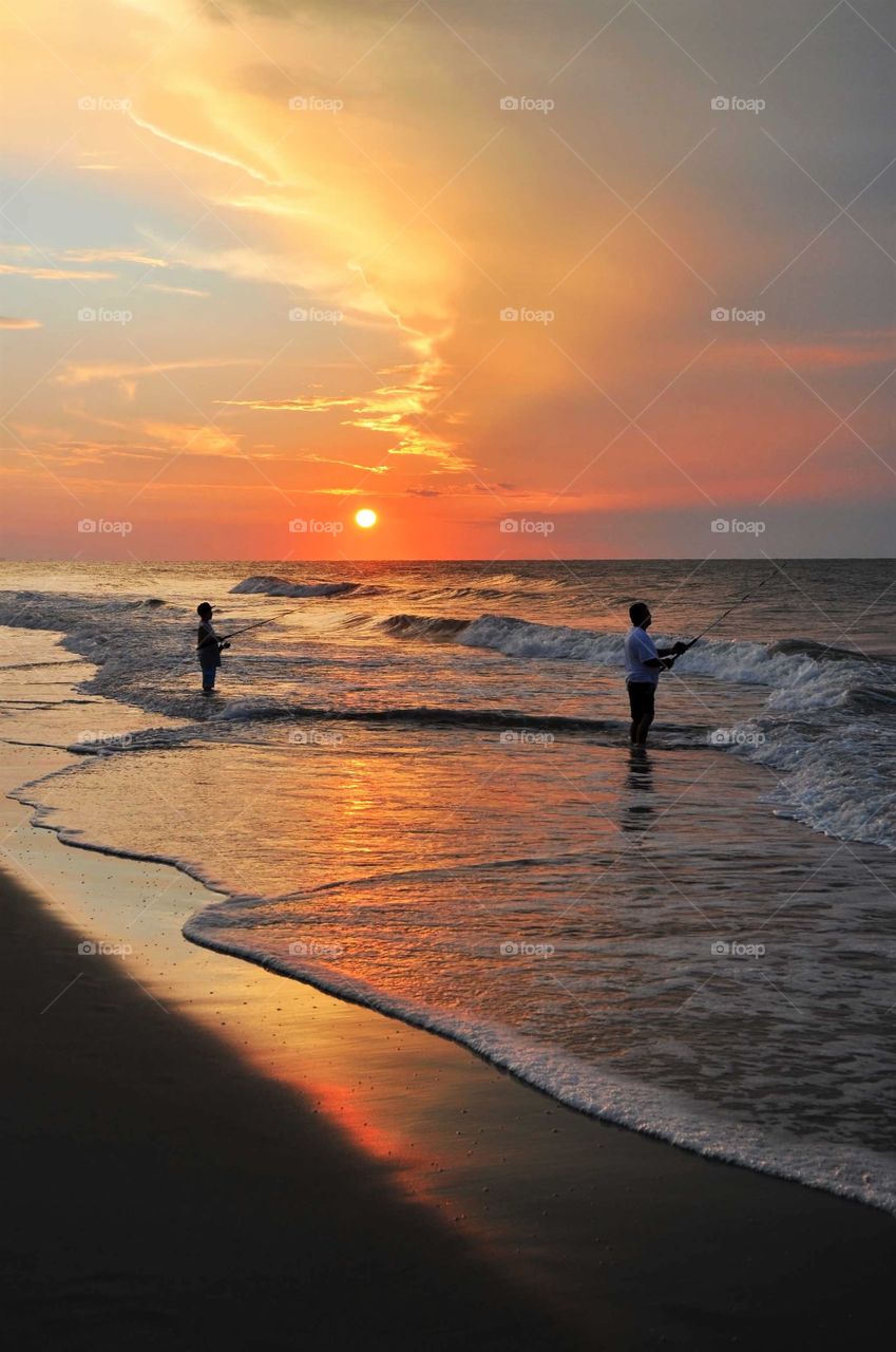 Silhouette of a young boy and his Father surf fishing at Sunrise In Myrtle Beach South Carolina. 