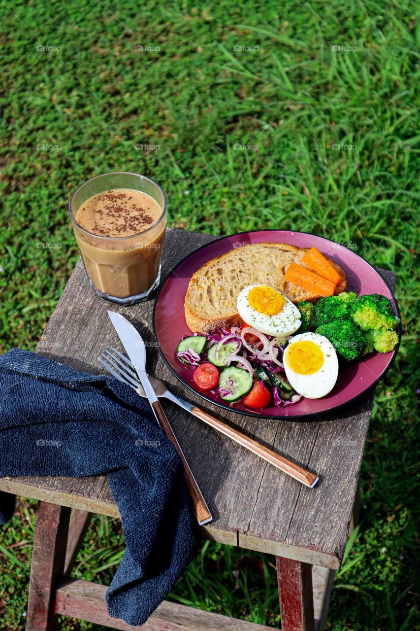 Early outdoor breakfast. A cup of hot coffee and a plate of healthy food, toast, some veggies and hard boiled egg 