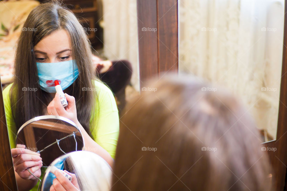 A young girl does makeup for a walk outside in a protective mask against the coronavirus pandemic, her lips are painted with red lipstick.