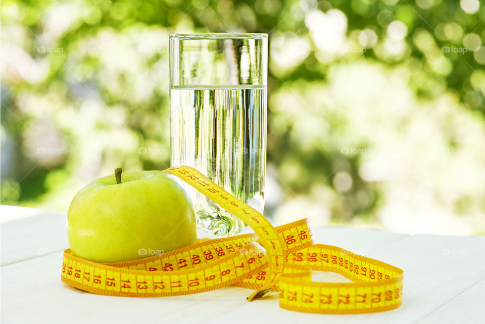 Diet. A apple with water and measuring tape on a white wooden table on green natural background. Health care concept