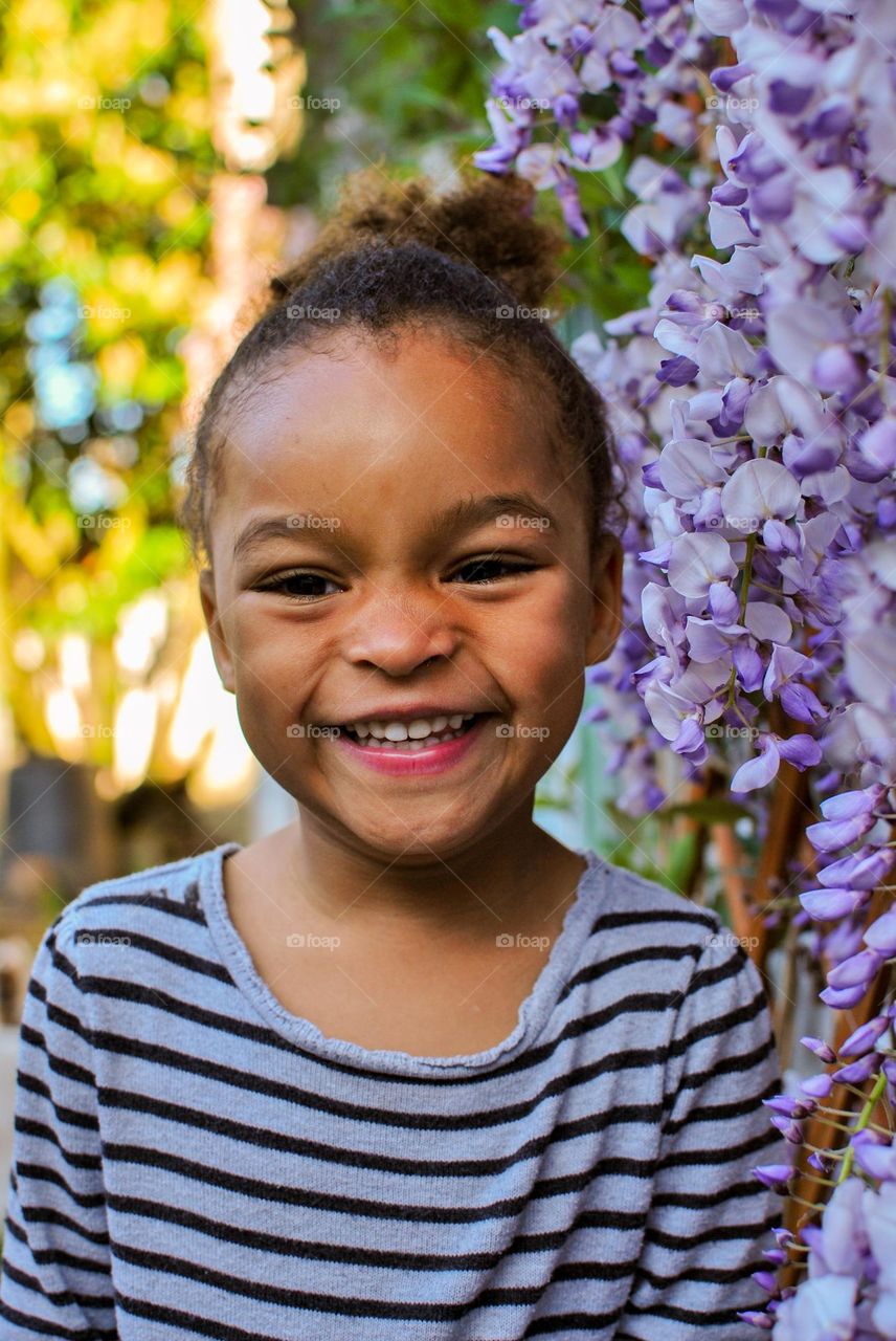 Smiling young adorable toddler in front of wisteria flowers