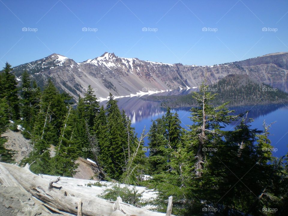 snow-capped mountain peaks and green trees bordering Crater Lake and Wizard Island in Oregon