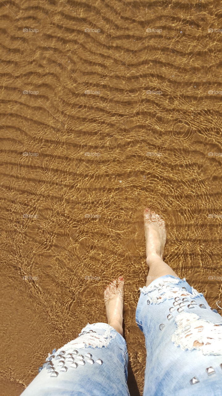 Selfie of feet entering in water on the beach, shot from above