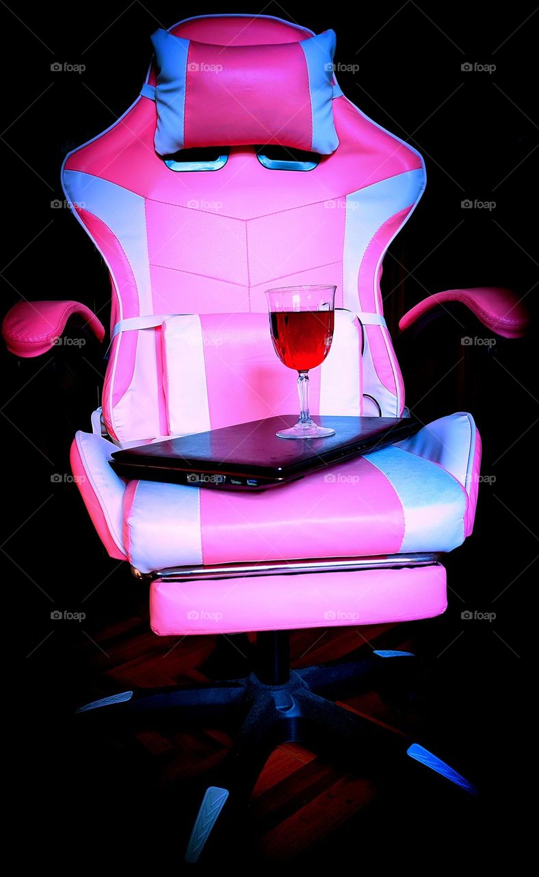 Barbie style.  On a black background, a pink computer chair.  There is a laptop on the chair with a glass of red wine on it
