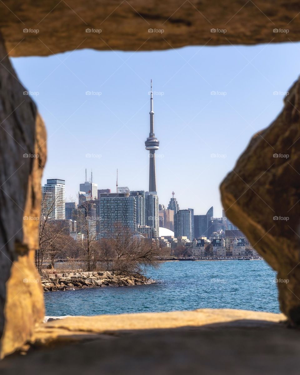 The CN tower in the Toronto skyline framed between rocks getting hit with golden sunlight 