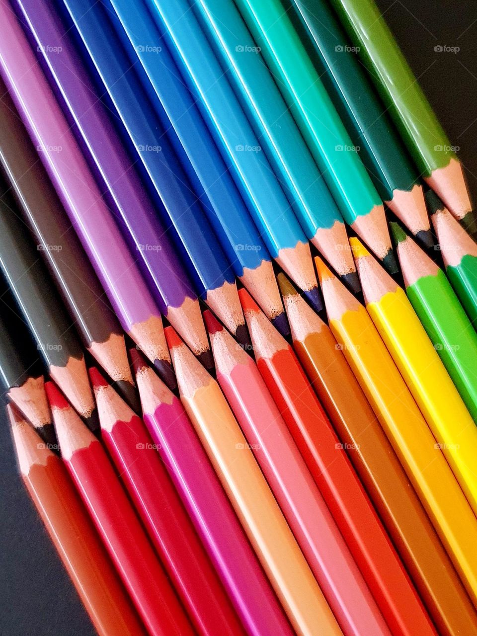 Colourful flatlay composition made of coloured pencils placed on a black paper creating a colour explosion