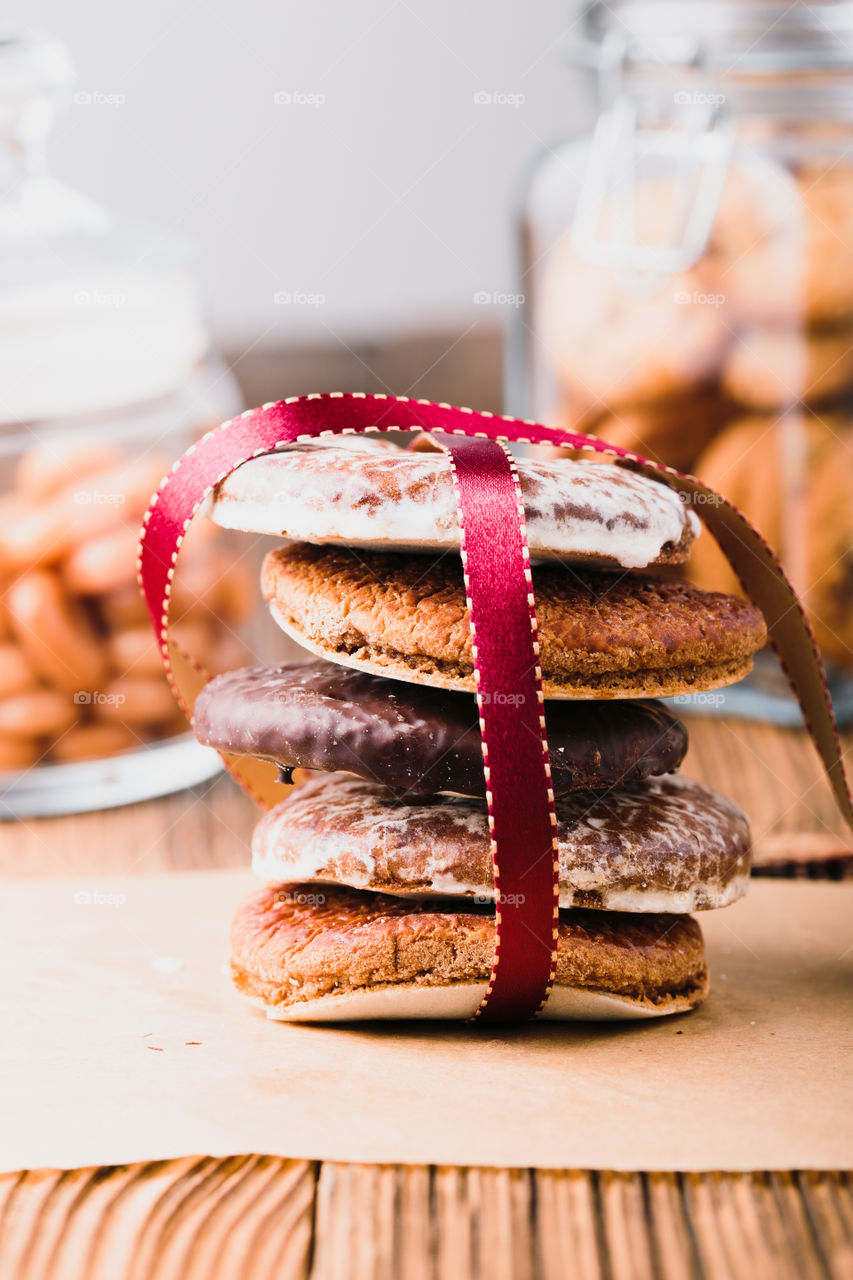 A few gingerbread cookies wrapped in red ribbon Happy Christmas on wooden table. Jars with sweets in the background