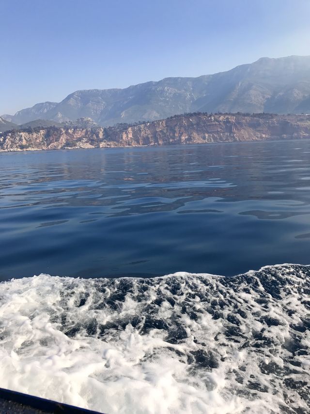 Clear blue water and white waves and big mountains in the back, in the sea, in the state of Montenegro, during the boat ride. 