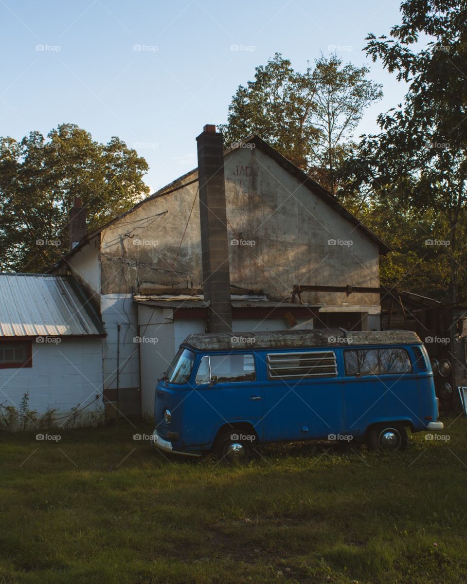 Rural scene at golden hour of an old VW Bus backdropped by an abandoned barn 