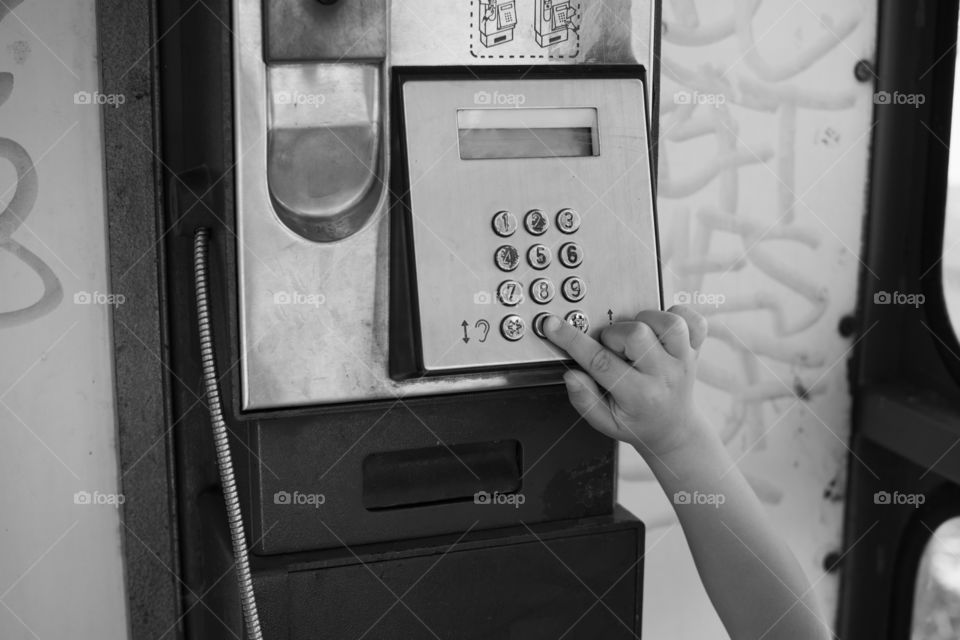 kid's hand typing numbers in telephone booth, dialing number