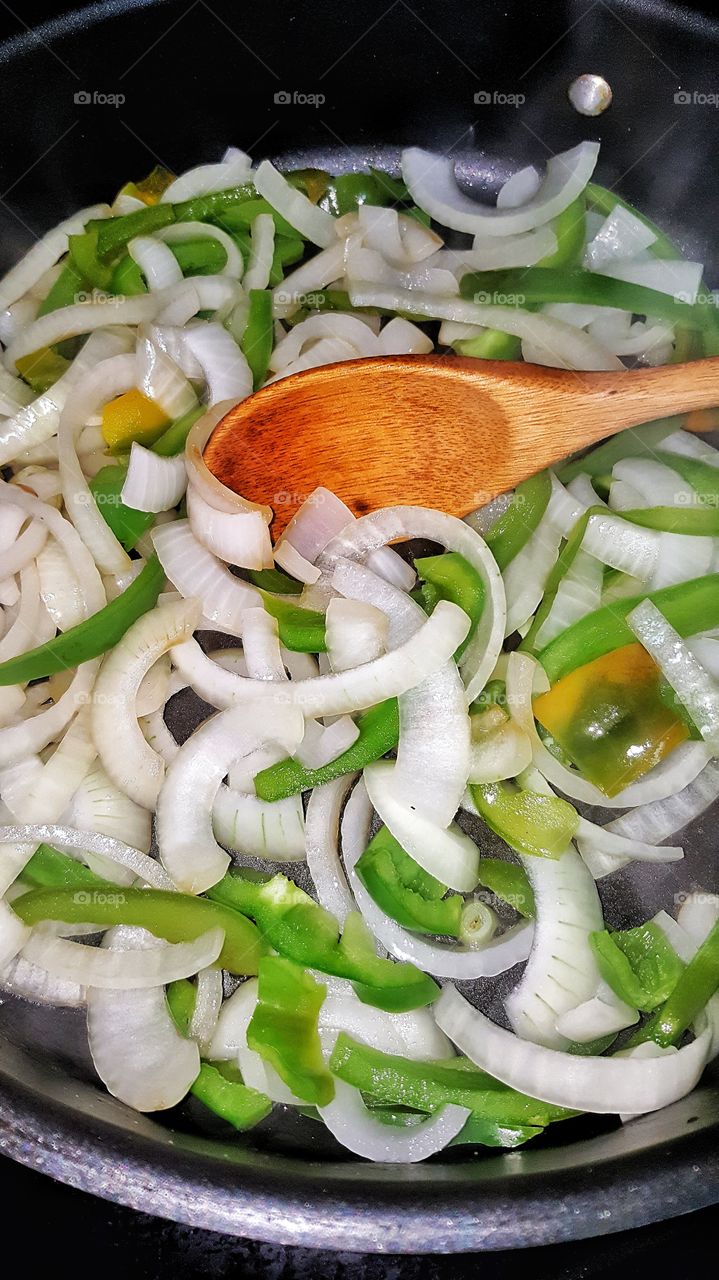 cooking onions and green peppers in skillet with wooden spoon