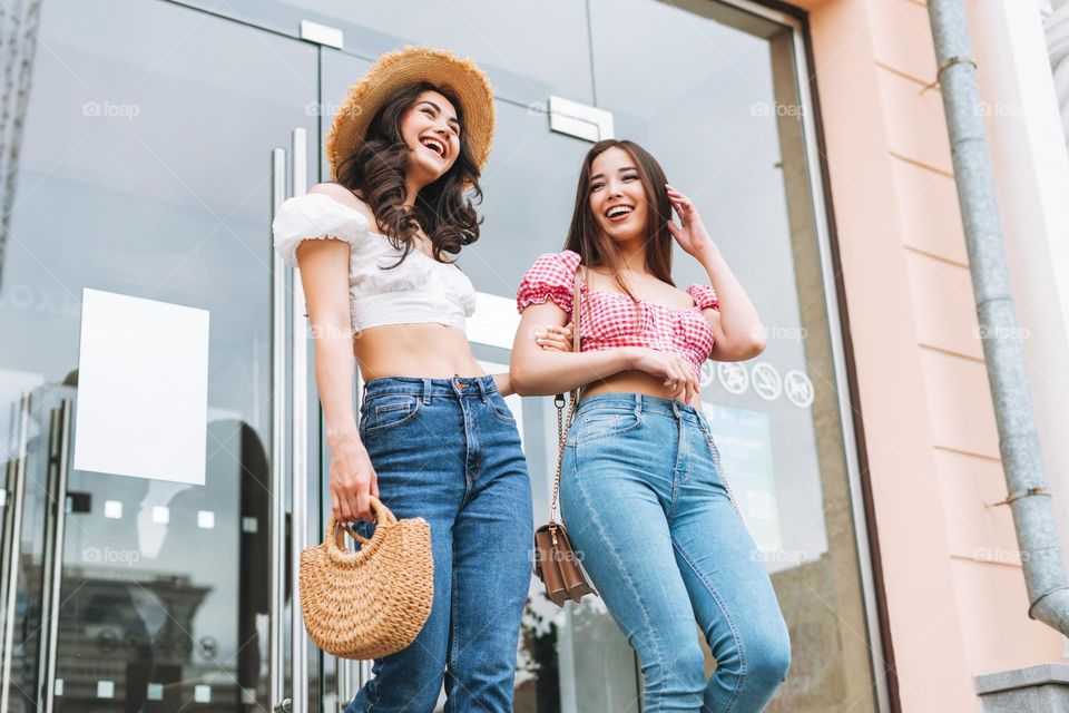 Happy smiling beautiful brunette young women friends in summer clothes walking on the summer city street, retail shopping