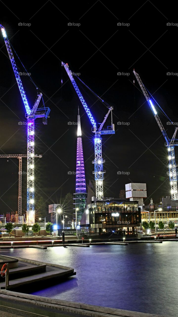tower cranes brightly lighting up the night sky, towering over the iconic bell tower in Perth, Western Australia