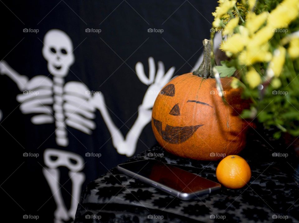 Decoration for Halloween.  A big pumpkin in the form of a winking emoticon and a skeleton next to a pumpkin and a phone