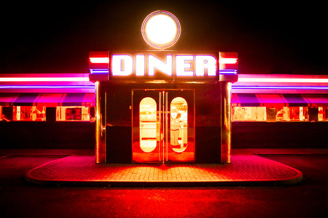 The doorway and entrance to a traditional American diner with brightly coloured neon lights fluorescent colours at night
