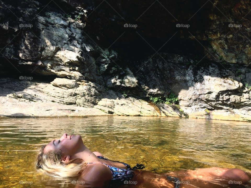 Blonde girl in bikini at a water. Beautiful hiking location with rocks and waterfalls. 