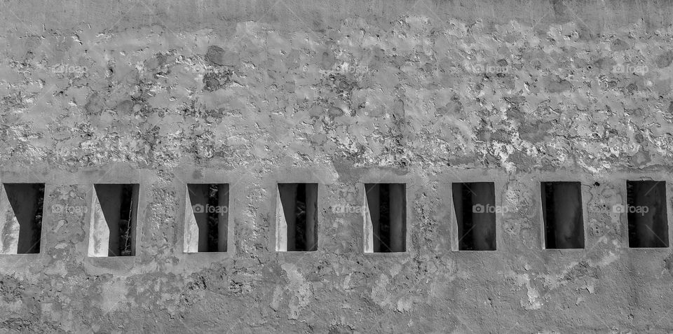 Beautiful view of the ancient wall with small square windows on a sunny day in the city of Cullera in Spain, close-up side view. Concept detailed architecture of medieval castles.