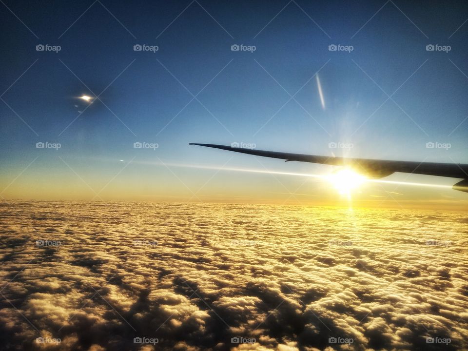photo from a plane , above the clouds with sun behind the wing