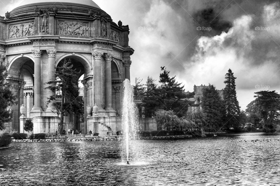 Vintage looking black and white image of the landmark Palace of Fine Arts in San Francisco California with the fountain rising through the lagoon on a warm sunny afternoon with clouds in the sky