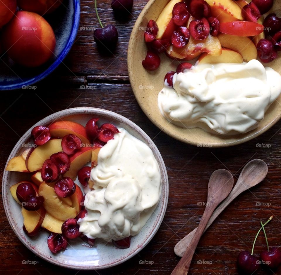 Chopped peaches and cherries with vanilla ice cream on plates with spoons sitting on a rustic wood table.
