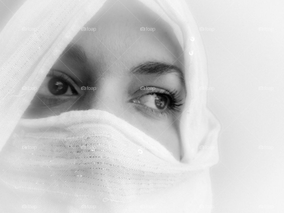 Black and white portrait of a woman covered in a white scarf during the pandemic, looking away in concern.  White background.