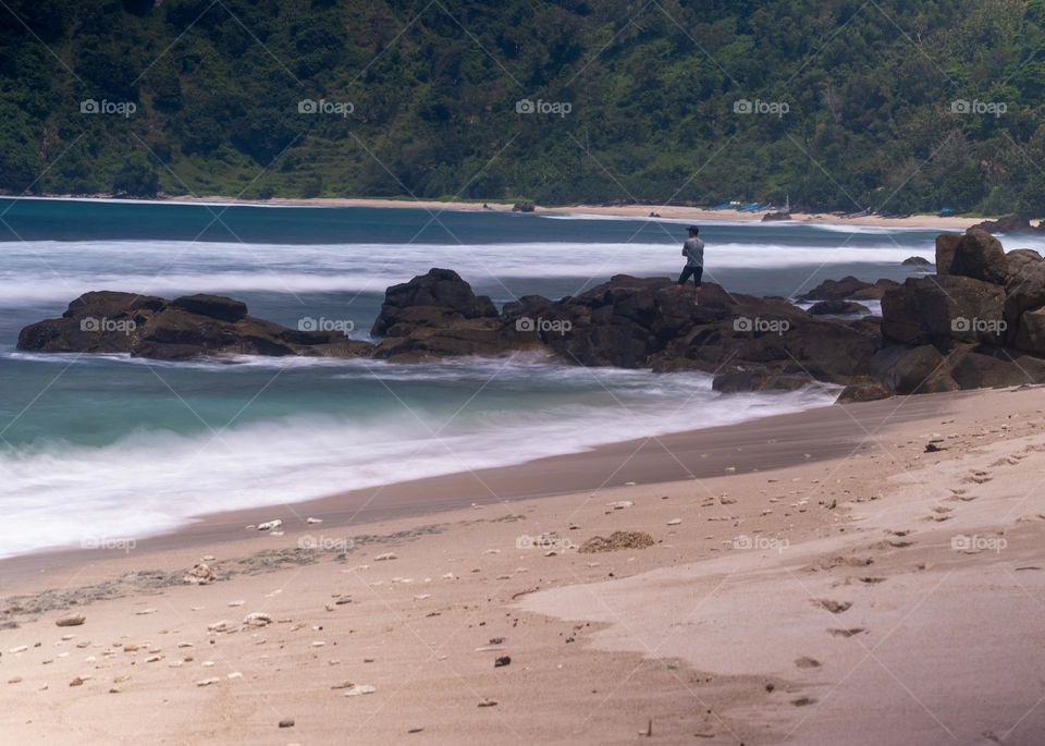 a man standing on a rock by the beach looking at the beauty of the sea