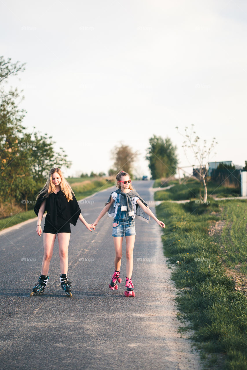 Teenage smiling happy girls having fun rollerskating, spending time together on summer day. Teenage smiling happy girls having fun walking outdoors, hanging, spending time together on summer day. Real people, authentic situations