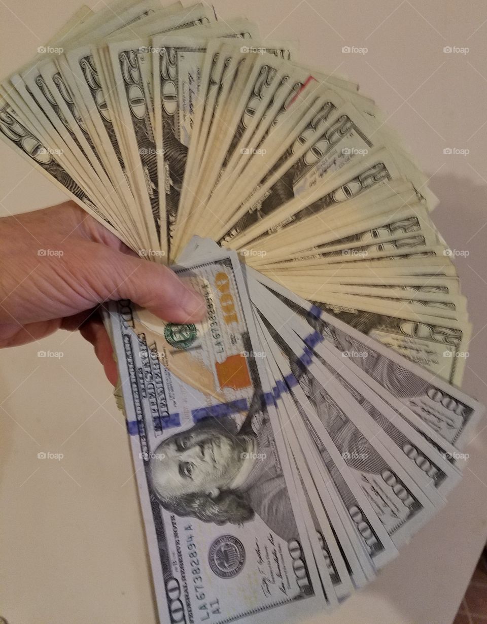 Hand holding fan of $20s & $100s paper bills U.S. currency.