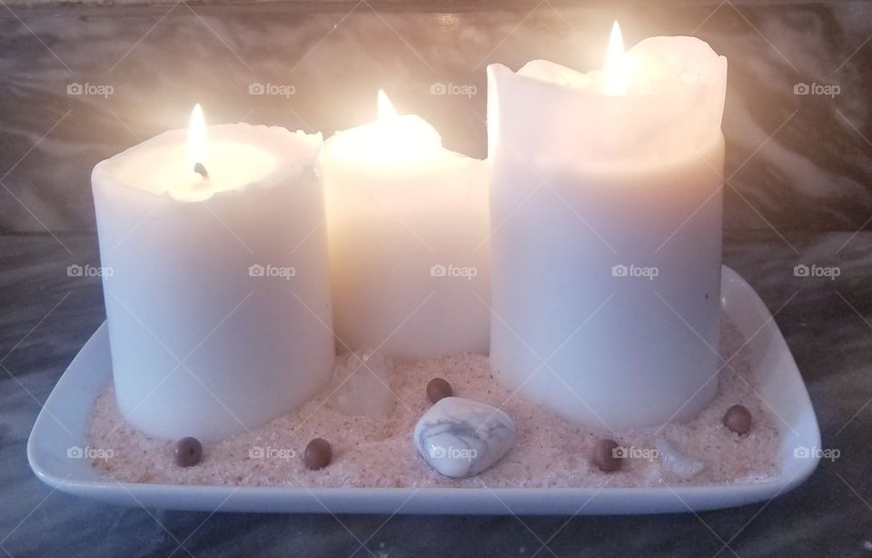 Three white pillar candles resting in a bed of pink Himalayan sea salt surrounded by clear quartz, howlite, and sandalwood beads
