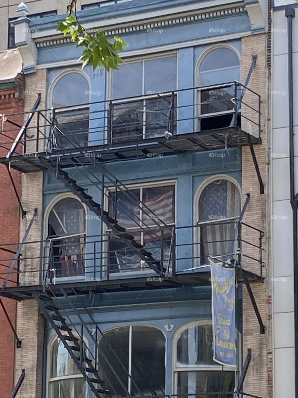 An old brick wall painted blue with rusted metal fire escapes and arched windows