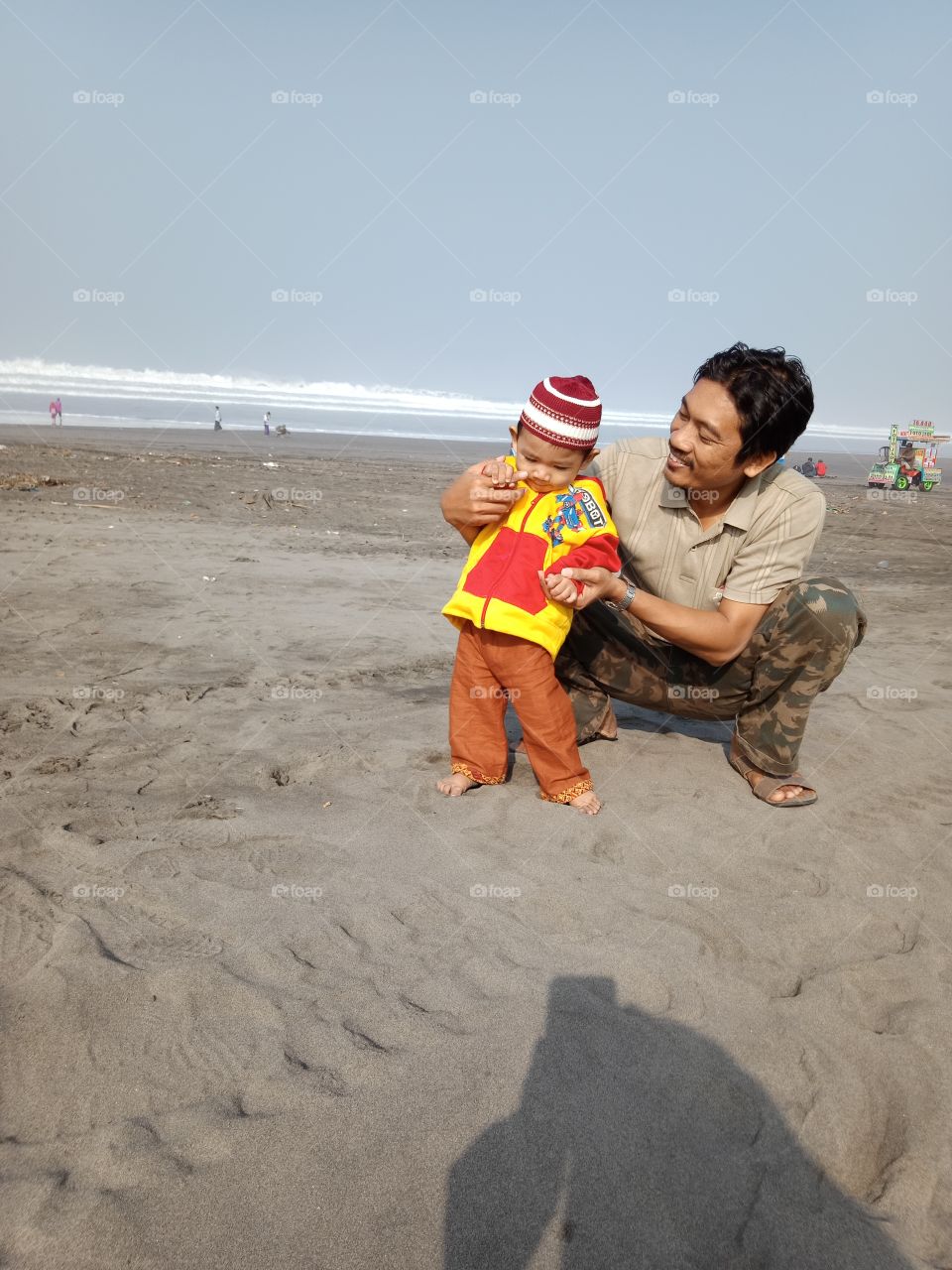 a baby boy learns to walk with his father on the beach