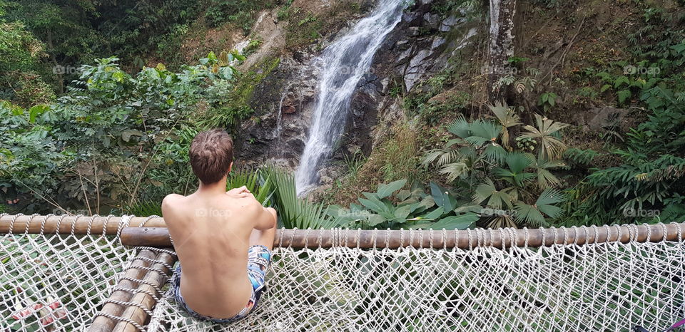 Man sitting on a hammock relaxing next to a waterfall