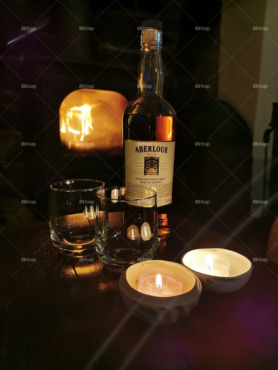 Aberlour Single malt whisky in front of a woodburning stove fire with candles and glasses on a wooden table