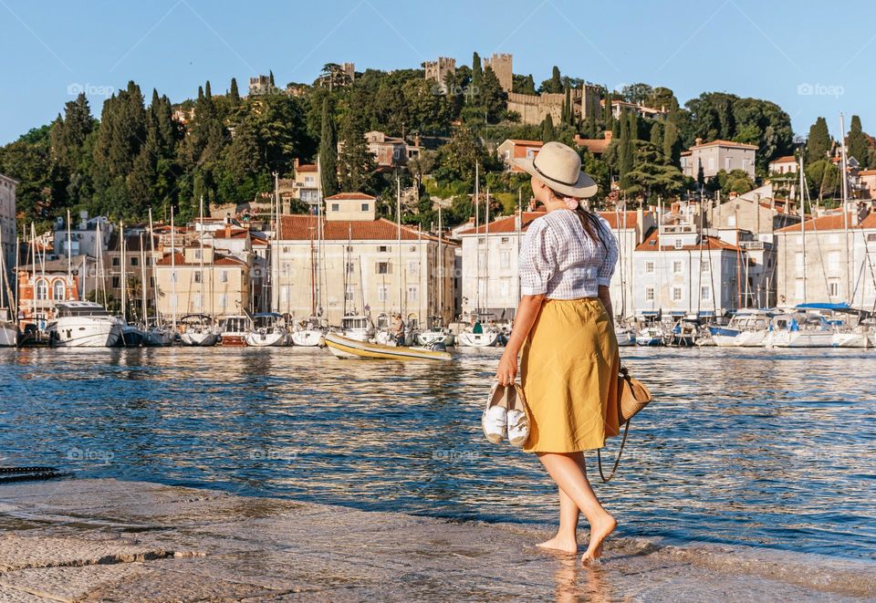 Rear view of woman wearing summer clothes and sunhat exploring the beautiful coastal town of Piran in Slovenia during summer