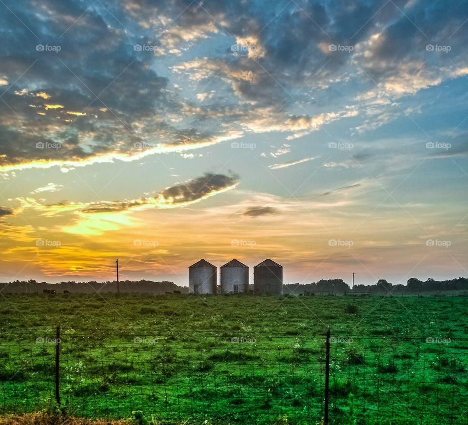 country sunrise behind three grain bins