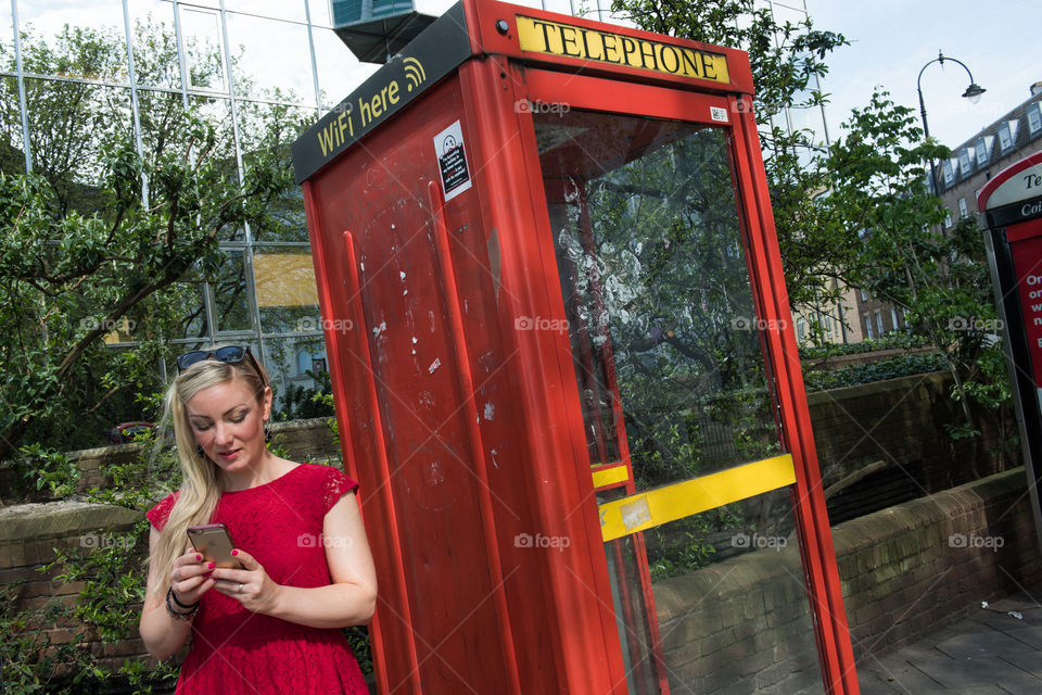 Woman standing near telephone booth holding mobile phone