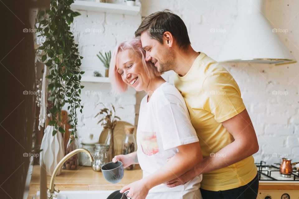 Young beautiful couple happy family having fun and wash dishes in bright kitchen at home