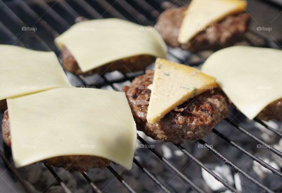 Mouthwatering burgers on charcoal grill topped with cheddar cheese and blue cheese