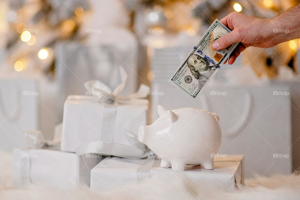 piggy bank with 100 dollars banknote in festive New Year atmosphere of scenery.  Magical bokeh with Christmas tree and bright lights.