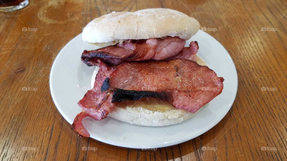 A white bun loaded with grilled bacon on a white plate screaming eat me