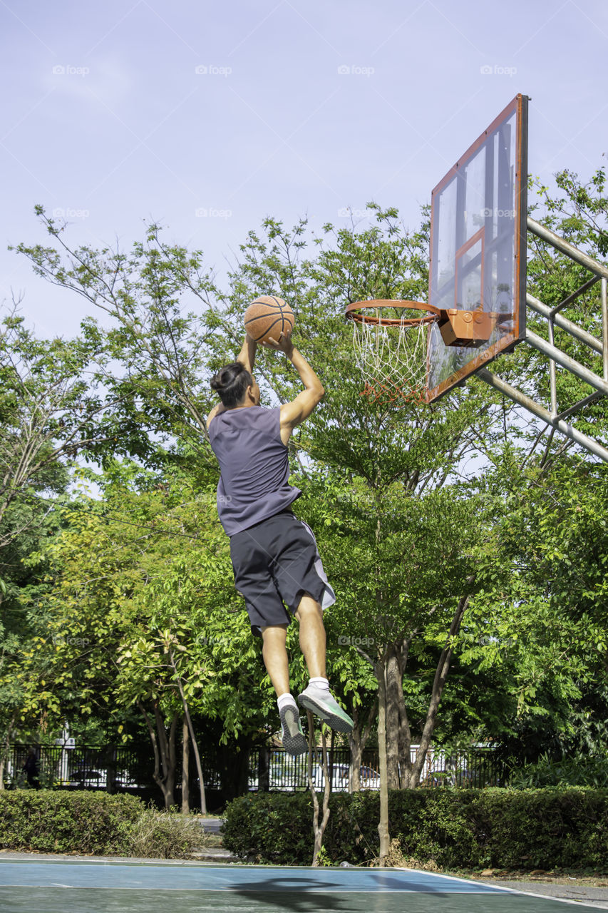 Basketball in hand man jumping Throw a basketball hoop Background  tree in park.