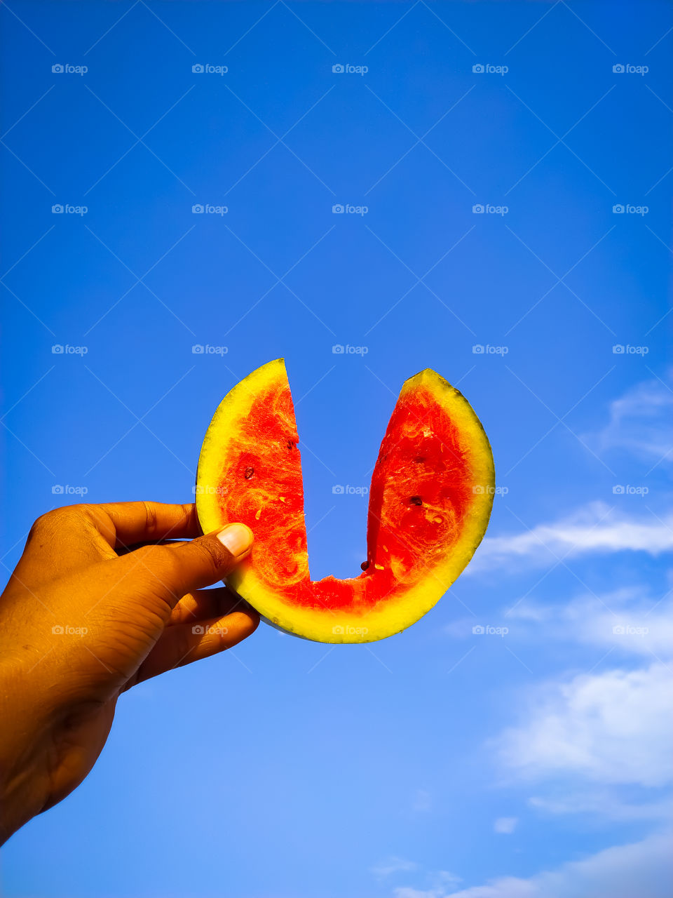 hand holding slice of watermelon on the blue sky
