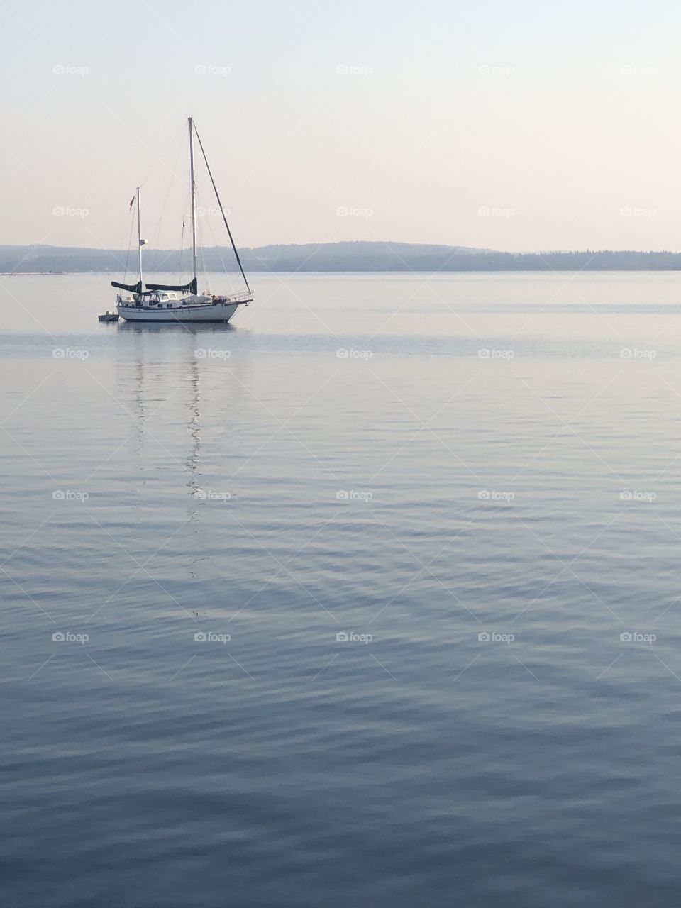 Sail boat on water. Sky, boat, and water are all soft blue hues.