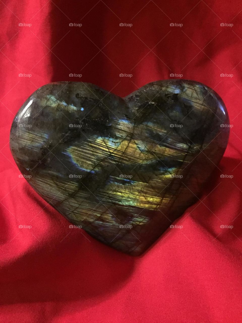 A shimmering Labradorite heart with a red background.