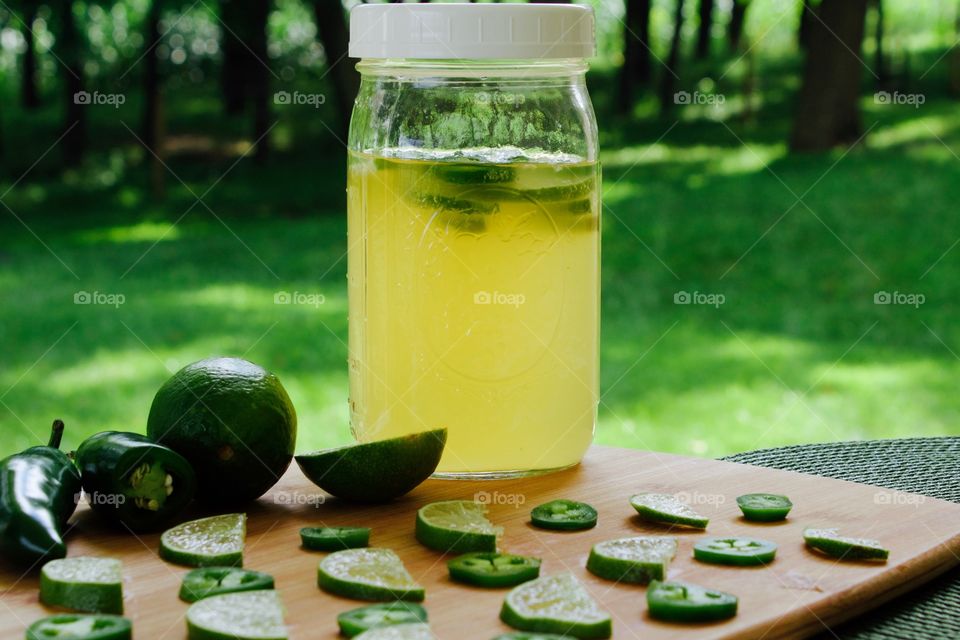 Refeshing lime-and-jalepeño-flavored kombucha, rebottled in a quart-size mason jar for a second ferment, with slices of lime and jalepeño on a bamboo cutting board, against a blurred outdoor background in summer