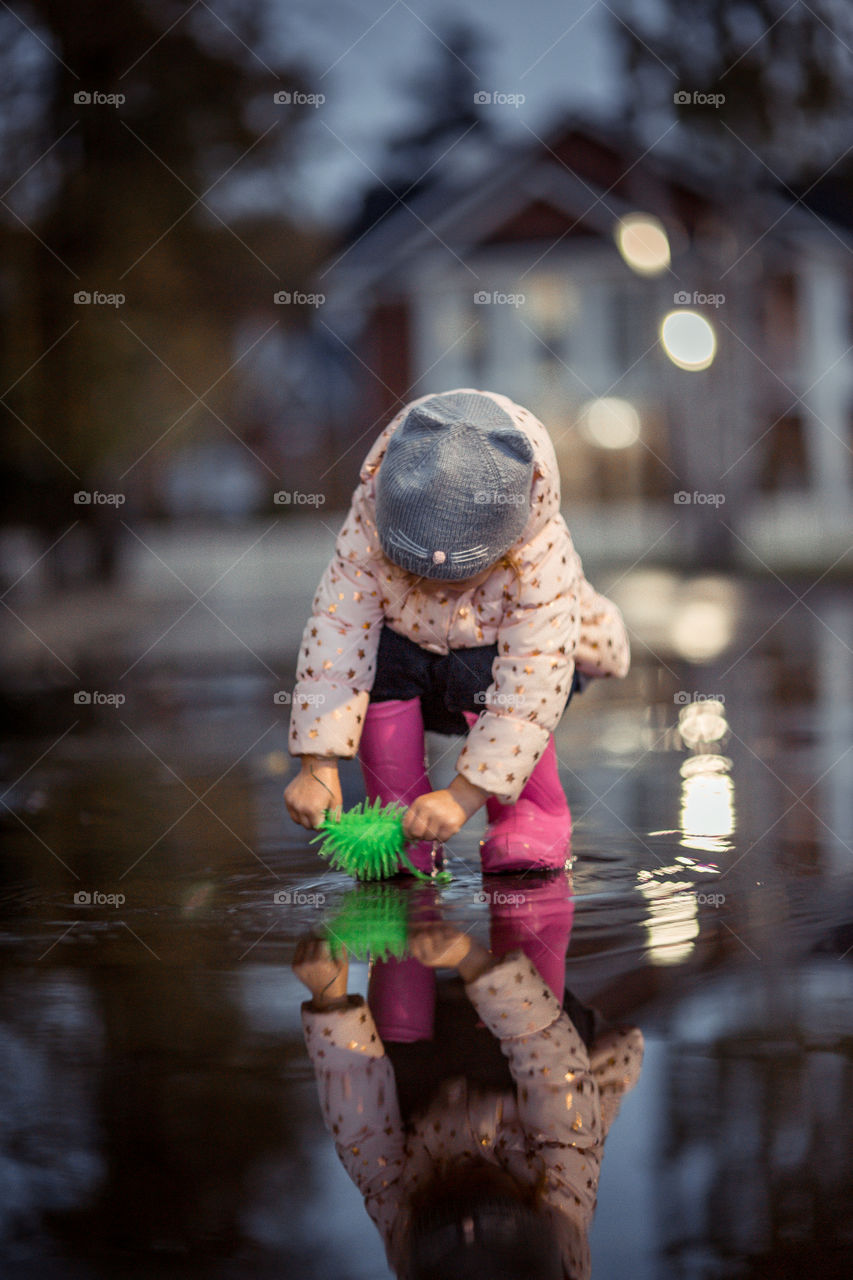 Little girl  in waterproof boots playing in a puddle 