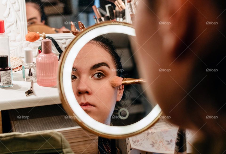 Portrait of young woman doing her make-up in front of circular led illuminated mirror