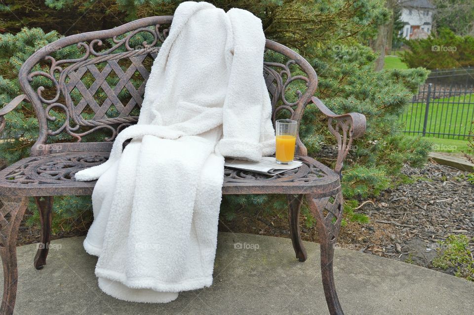 White bathrobe laid out on a bench outdoors with newspaper and juice