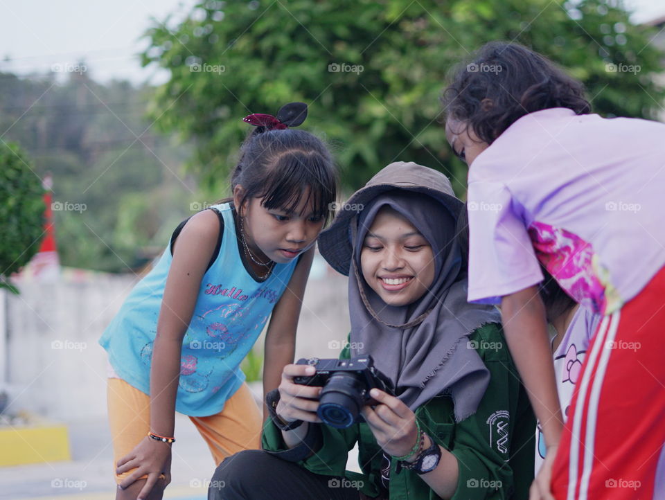 A girl is showing a picture in the camera to the local children who don't understand so much about technology.