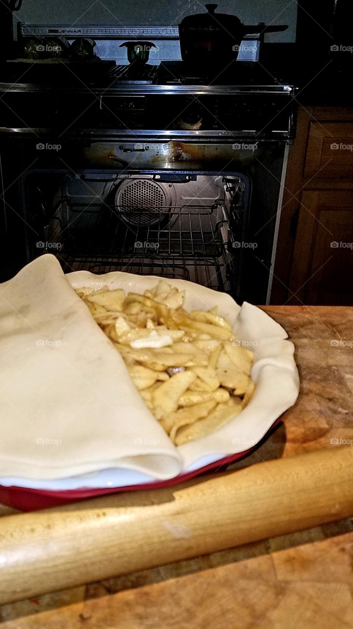Uncooked but ready for oven baking, apple pie before top crust laid flat & crimped. Open oven in background.